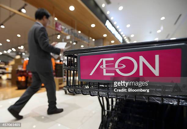 Man walks past a shopping cart bearing the Aeon Co. Logo at the Aeon Mall Makuhari Shintoshin shopping mall, operated by Aeon Mall Co., during a...
