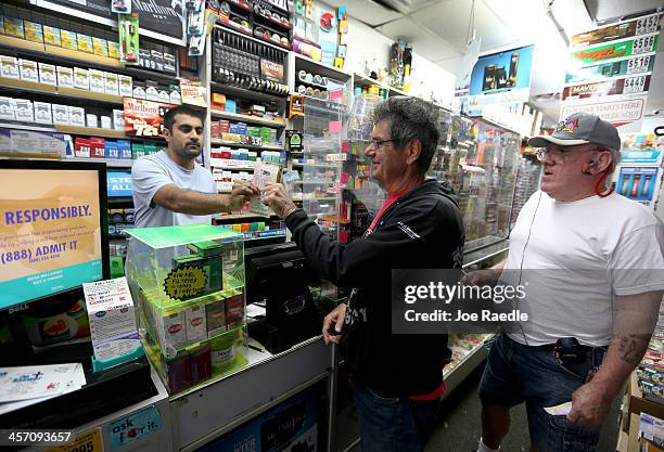 Frank Butera and David Talvis purchase their Mega Million lottery tickets from Hiral Patel at Circle News Stand on December 16, 2013 in Hollywood,...