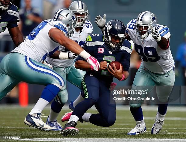 Quarterback Russell Wilson of the Seattle Seahawks slides to the turf as defensive end Tyrone Crawford, defensive end Anthony Spencer and defensive...