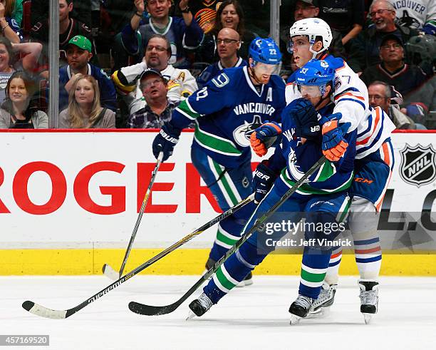 Daniel Sedin of the Vancouver Canucks looks on as David Perron of the Edmonton Oilers checks Henrik Sedin of the Vancouver Canucks during their NHL...