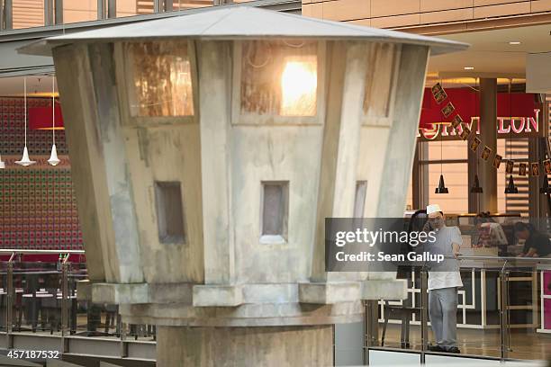 Cook from a nearby Asian fast food restaurant talks on a mobile phone while standing near the mock-up of an East German guard tower like those that...