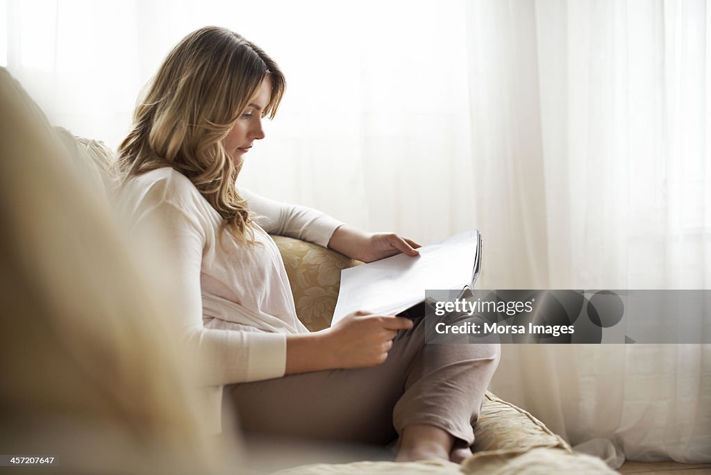 Woman sitting on sofa reading magazine