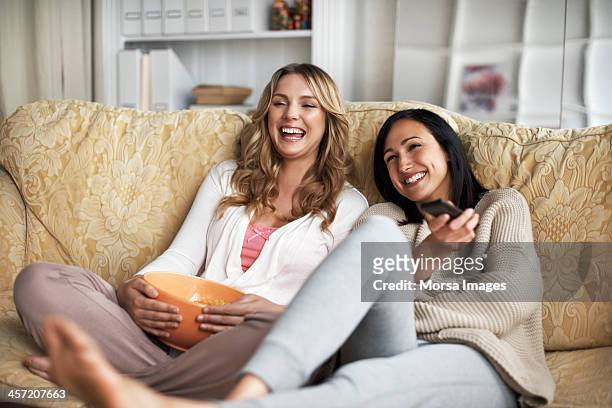 woman sitting on sofa watching tv - women laughing stock pictures, royalty-free photos & images