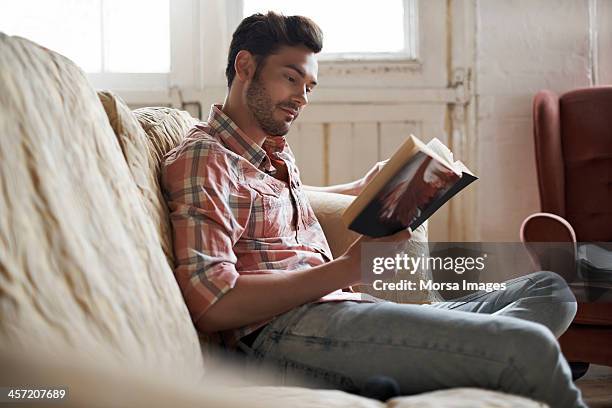 man sitting on sofa reading a book - reading book stockfoto's en -beelden