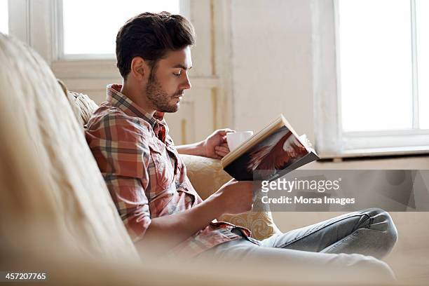 man sitting on sofa reading book - lezen stockfoto's en -beelden