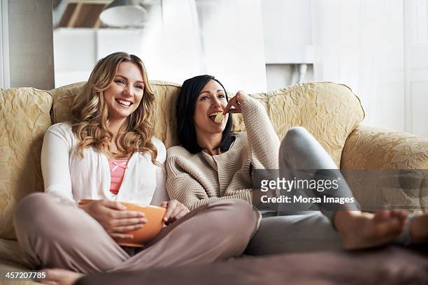 women sitting on sofa watching a movie - vriendin stockfoto's en -beelden