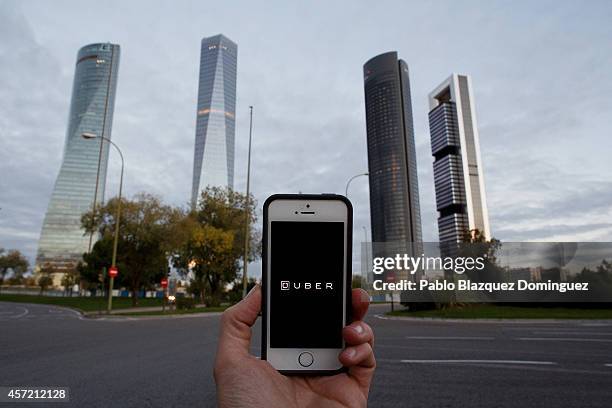 In this Photo Illustration a smart phone displays a picture with the logo of the news taxi app 'Uber' near the Cuatro Torres 'Four Towers' business...