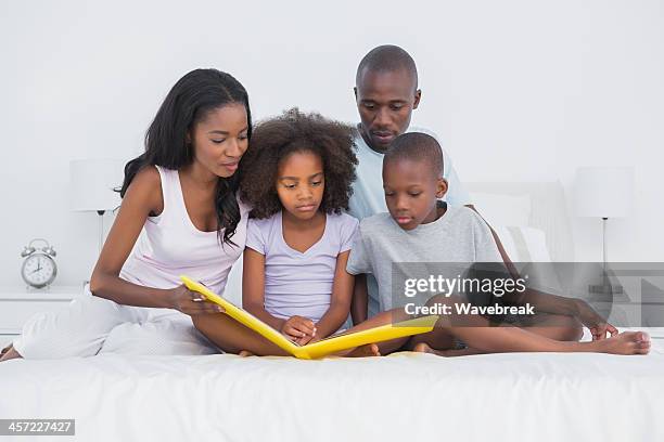 glückliche familie sitzt auf dem bett, blick auf ein fotoalbum - looking at a photo album stock-fotos und bilder
