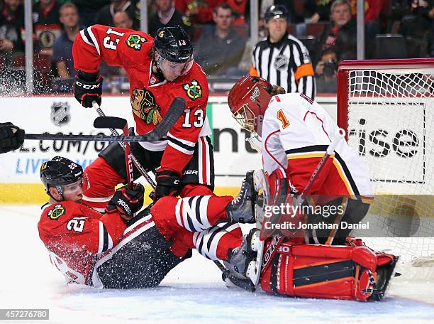 Ben Smith of the Chicago Blackhawks collides with Jonas Hiller of the Calgary Flames as Daniel Carcillo tries to dig out the puck at the United...