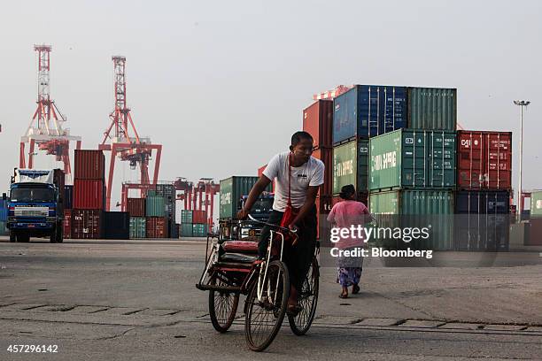 Man rides a rickshaw pasts stacked containers as cranes stand in the background at the Myanmar Industrial Port in Yangon, Myanmar, on Tuesday, Oct....