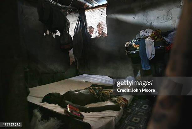 Family members peer into a bedroom as the dead body of a man awaits the arrival of an Ebola burial team to take him for cremation on October 17, 2014...