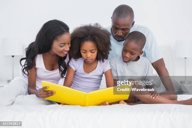 linda familia sentada en la cama mirando el álbum de fotos - album covers fotografías e imágenes de stock