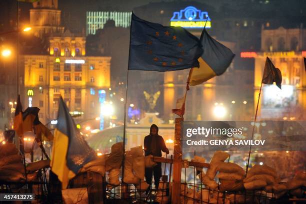 An activist stands atop a barricade flanked by the European Union and Ukrainian flags during an opposition rally on Independence Square in central...