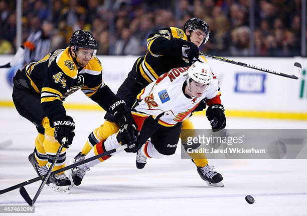Paul Byron of the Calgary Flames is hit by Torey Krug of the Boston Bruins while chasing down a puck in front of Dennis Seidenberg of the Boston...