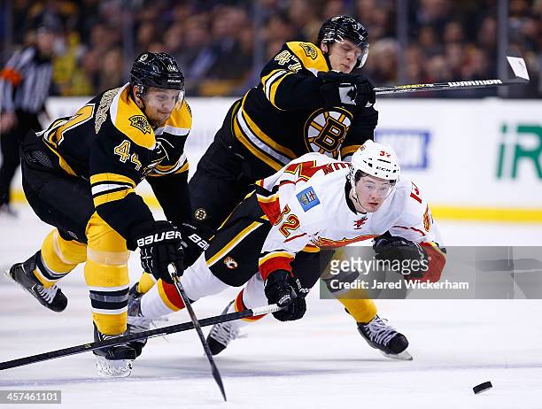 Paul Byron of the Calgary Flames is hit by Torey Krug of the Boston Bruins while chasing down a puck in front of Dennis Seidenberg of the Boston...