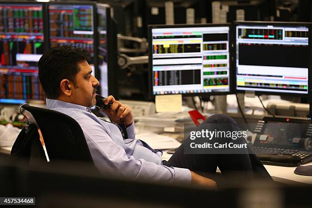 An employee talks on the phone as he views trading screens at the offices of Panmure Gordon and Co on October 20, 2014 in London, England. Markets...