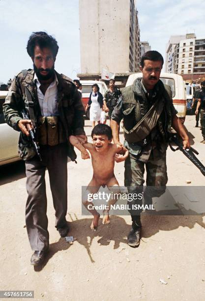 Shiite militiaman and a Lebanese soldier carry a Palestinian refugee boy out of Sabra Palestinian camp, in Beirut 28 May 1985, which has been taken...