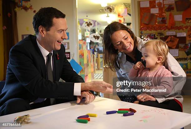 British Chancellor of the Exchequer George Osborne gestures to 18 month old Jessica Woodcock as she sits with her mother Lucy at the Toyota company...