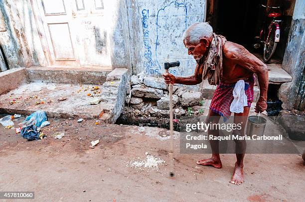 Elder man wearing only a lungi tries to walk the streets helped by a crutch.