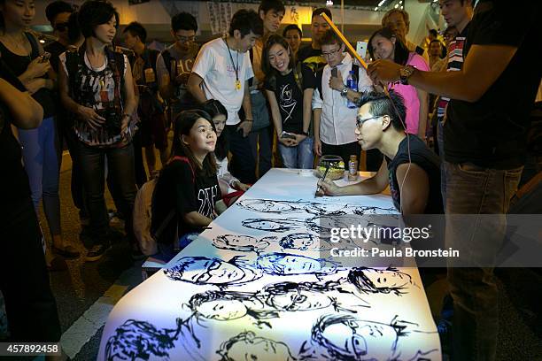 Hong Kong Artist Brian Chui who is a design consultant visiting from New York draws faces of the protest as a large mural at the main protest as a...