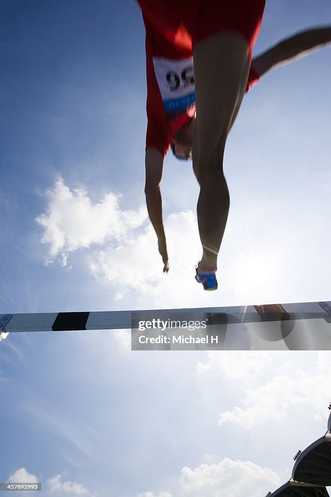 Male runner jumping hurdles in race