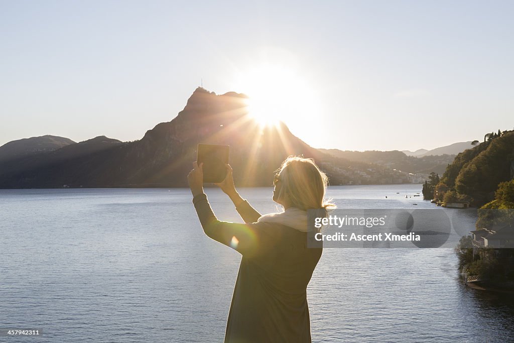 Woman takes picture with digital tablet above lake