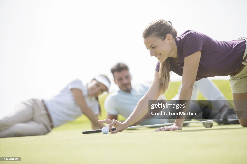 Friends watching woman flick golf ball toward hole