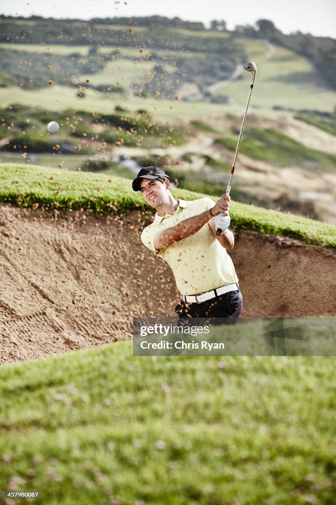 Man swinging from sand trap on golf course