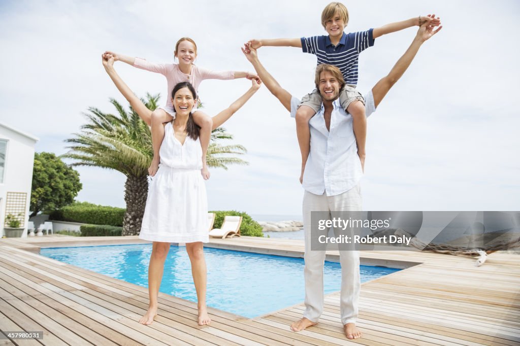 Parents carrying children on shoulders at luxury poolside