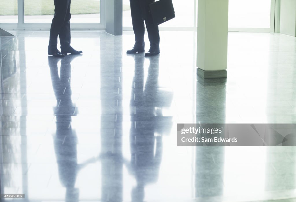 Reflection of businessmen shaking hands in office lobby