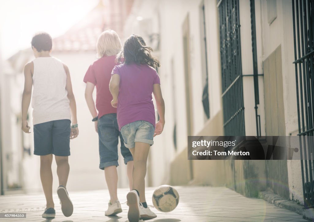 Children playing with soccer ball in alley