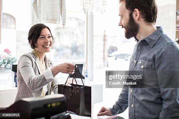 mid adult female design professional giving shopping bag to customer at cash counter in studio - fashion store staff stock pictures, royalty-free photos & images