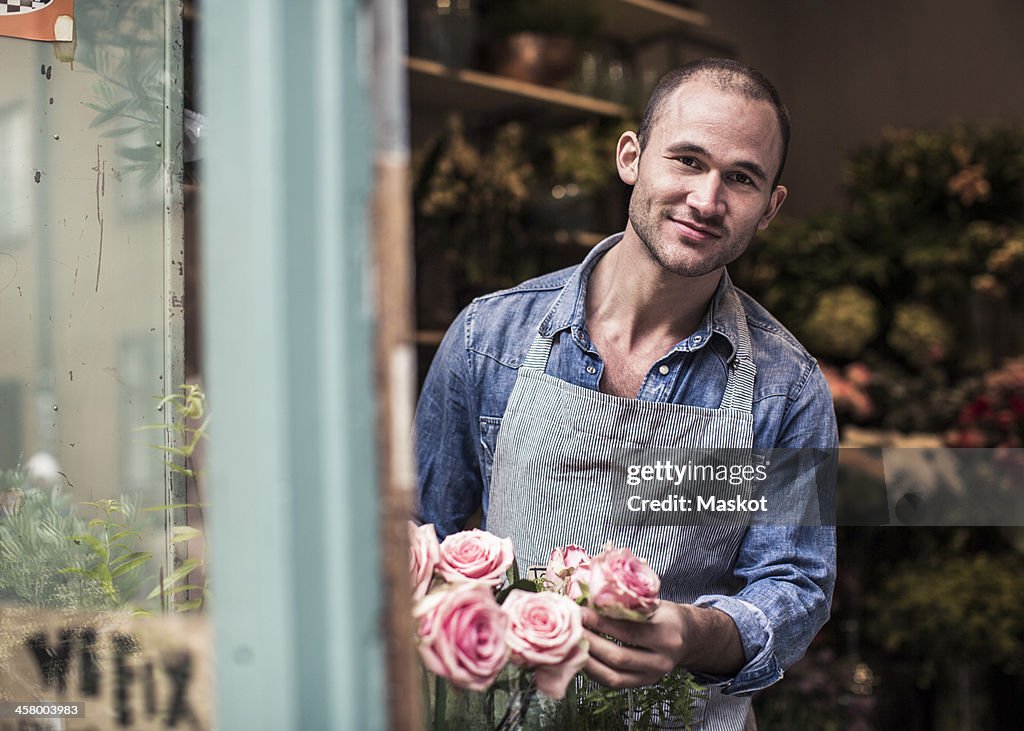 Portrait of happy male florist holding flowers while working at shop