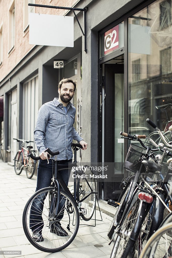 Portrait of happy mid adult male owner standing outside bicycle repair shop