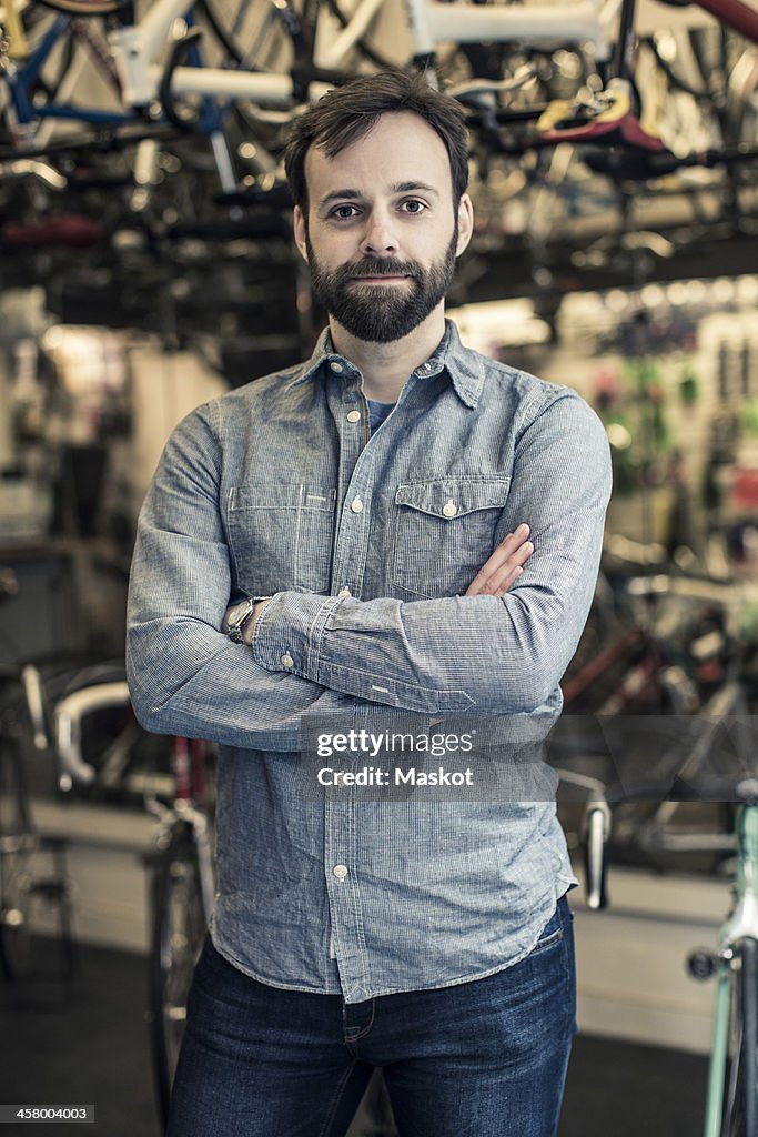 Portrait of confident mid adult male owner standing arms crossed at bicycle repair shop