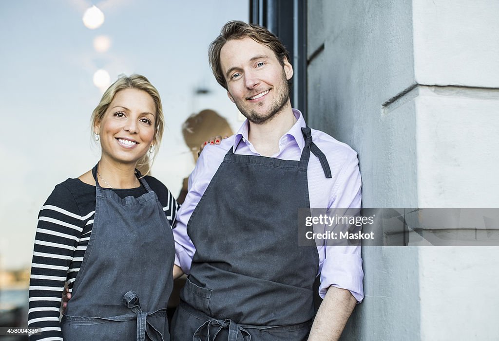 Mid adult confident owners standing at the entrance of restaurant