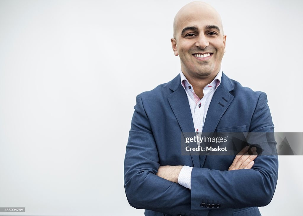 Portrait of mid adult businessman smiling while standing arms crossed against wall