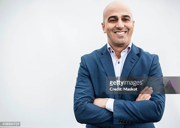 portrait of mid adult businessman smiling while standing arms crossed against wall - arab businessman stock pictures, royalty-free photos & images