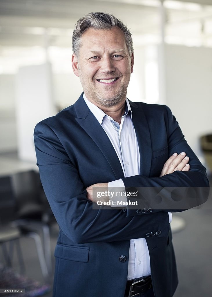 Portrait of happy mature businessman standing arms crossed in office