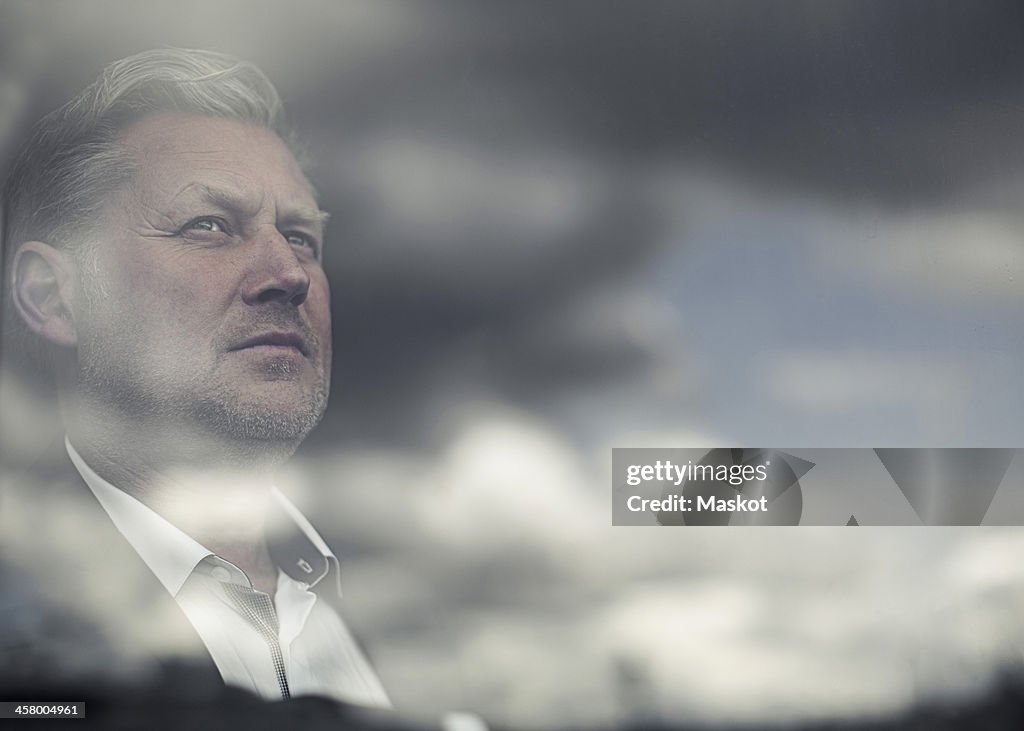 Reflection of clouds on glass window while businessman looking away