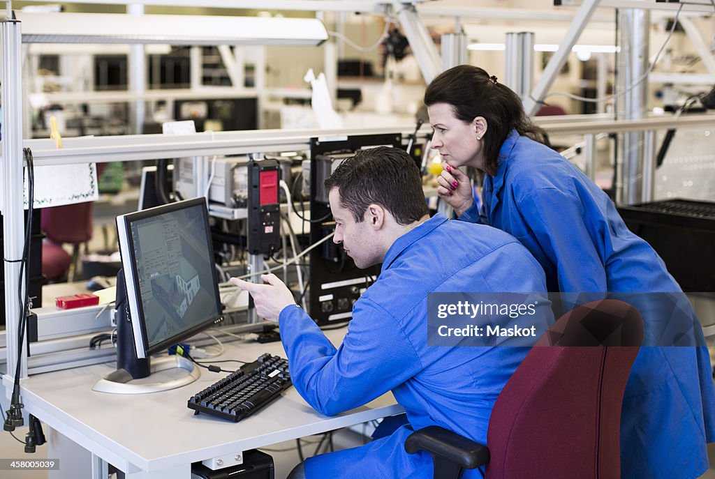 Male electrician pointing at computer monitor while discussing with colleague in industry