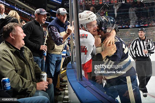 Fans watch as Mark Borowiecki of the Ottawa Senators and Jared Boll of the Columbus Blue Jackets fight against the glass during the first period on...