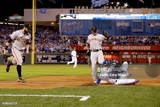 Alcides Escobar of the Kansas City Royals slides into first base safely in front of the tag of Brandon Belt of the San Francisco Giants as Joe Panik...
