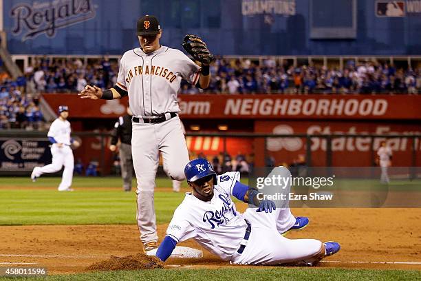 Alcides Escobar of the Kansas City Royals slides into first base safely in front of the tag of Brandon Belt of the San Francisco Giants as Joe Panik...