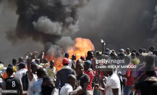 People stand in front of smoke rising from the Burkina Faso's Parliament, where demonstrators set cars on fire parked in a courtyard of the...