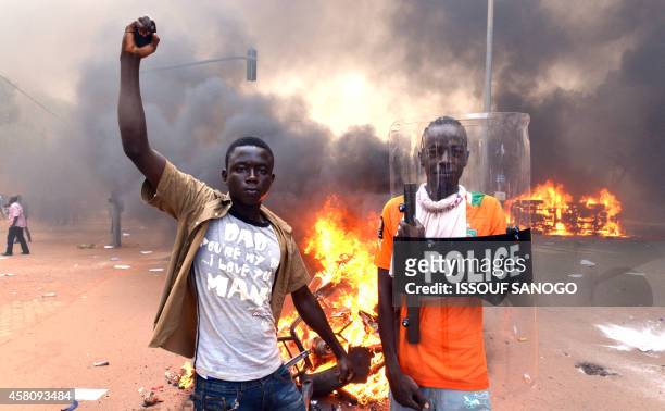Protesters pose with a police shield outside the parliament in Ouagadougou on October 30, 2014 as cars and documents burn outside. Hundreds of angry...