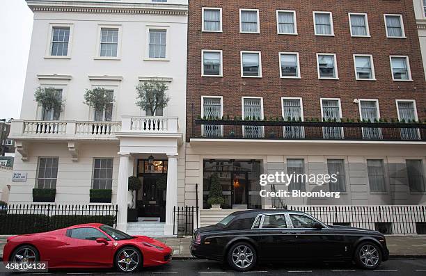 Red Ferrari luxury automobile and a black Rolls Royce car stand parked outside properties on Eaton Place in the Kensington district of London, U.K.,...