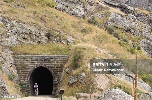 cyclist exits a tunnel on the otago rail trail - otago stock pictures, royalty-free photos & images