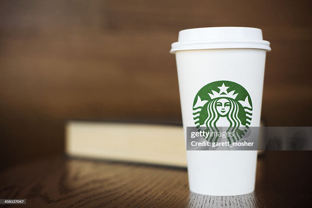 Grande Starbucks to go cup on wooden table with book