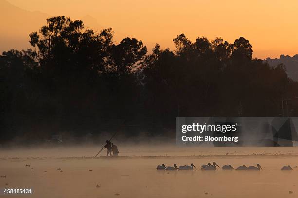 People steer a "trajinera", or gondola at dawn past one of the the artificial islands, known as "chinampas," on a canal at Lake Xochimilco in Mexico...